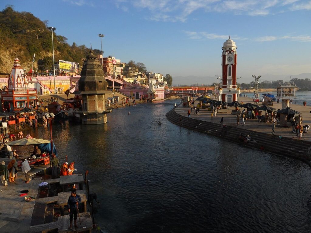 The ghat channel at Har Ki Pauri in low golden light, with the clock tower, temples and pilgrims along the water.