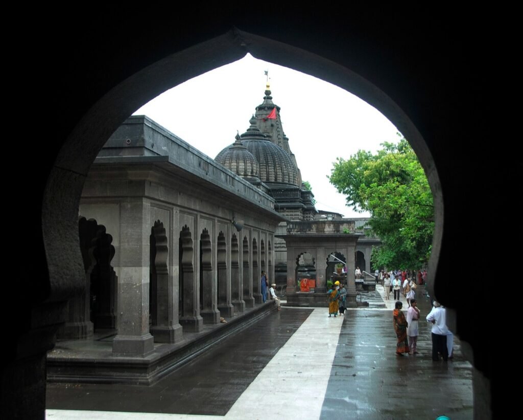 The black stone cloister of the Kalaram temple complex in Panchavati, seen through an arched gateway, with the temple spire and dome beyond.