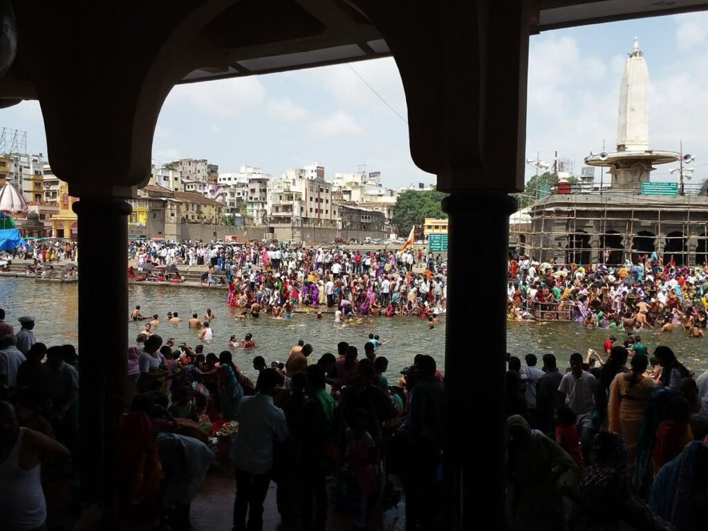 Pilgrims bathing at Ramkund on the Godavari in Nashik, seen through the arches of a riverside arcade