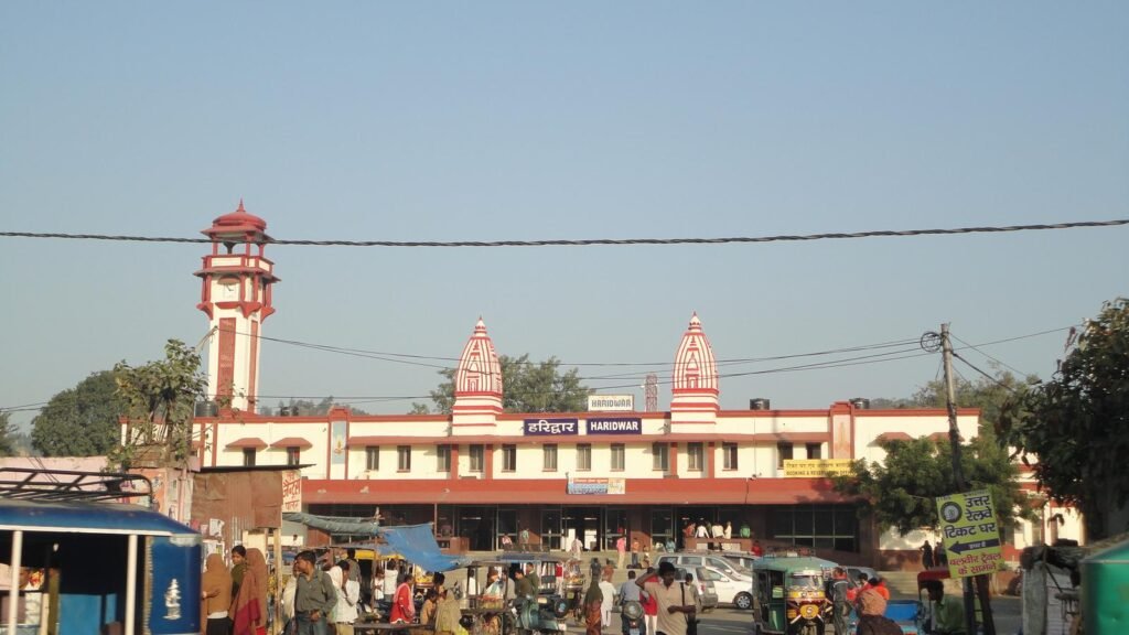 The front of Haridwar Junction railway station with its temple-style towers and a clock tower, with traffic outside.