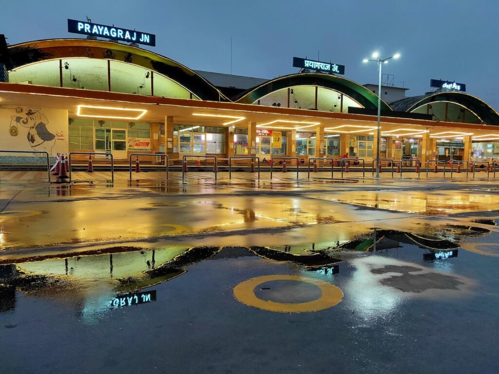 The front of Prayagraj Junction railway station reflected in rainwater on the forecourt in the evening.