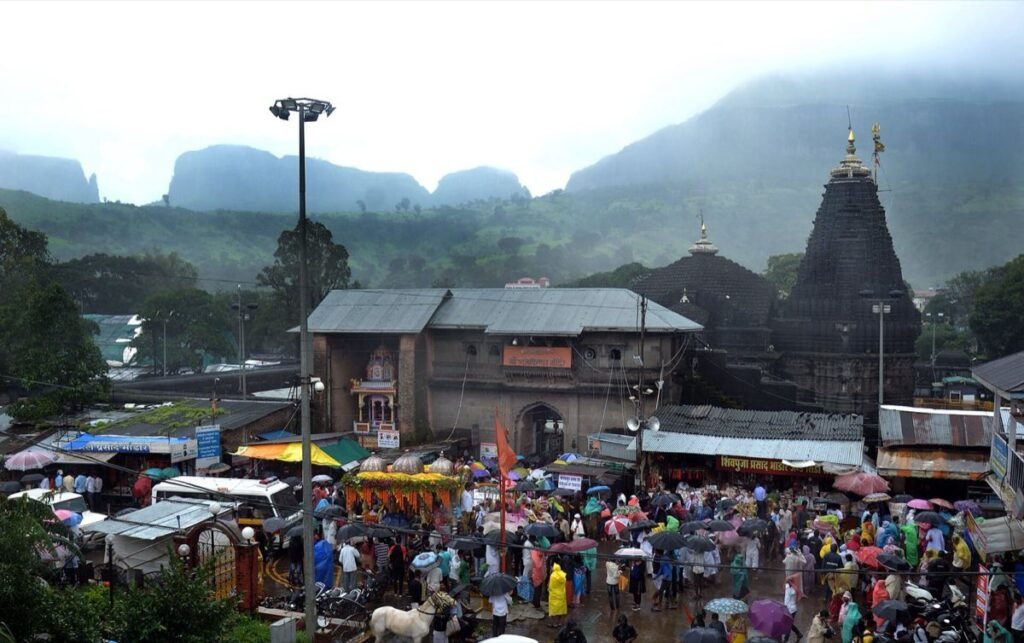 Trimbakeshwar Temple below the misty Brahmagiri hills, with pilgrims holding umbrellas in the square
