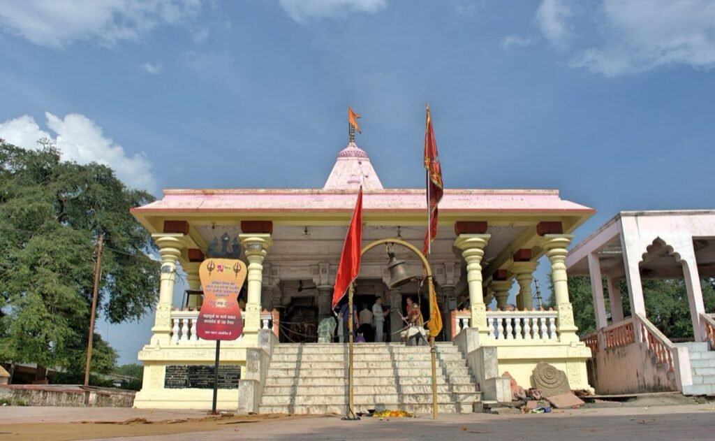 The pillared hall and pink shikhara of the Kal Bhairav Temple in Ujjain, with flags and a temple bell