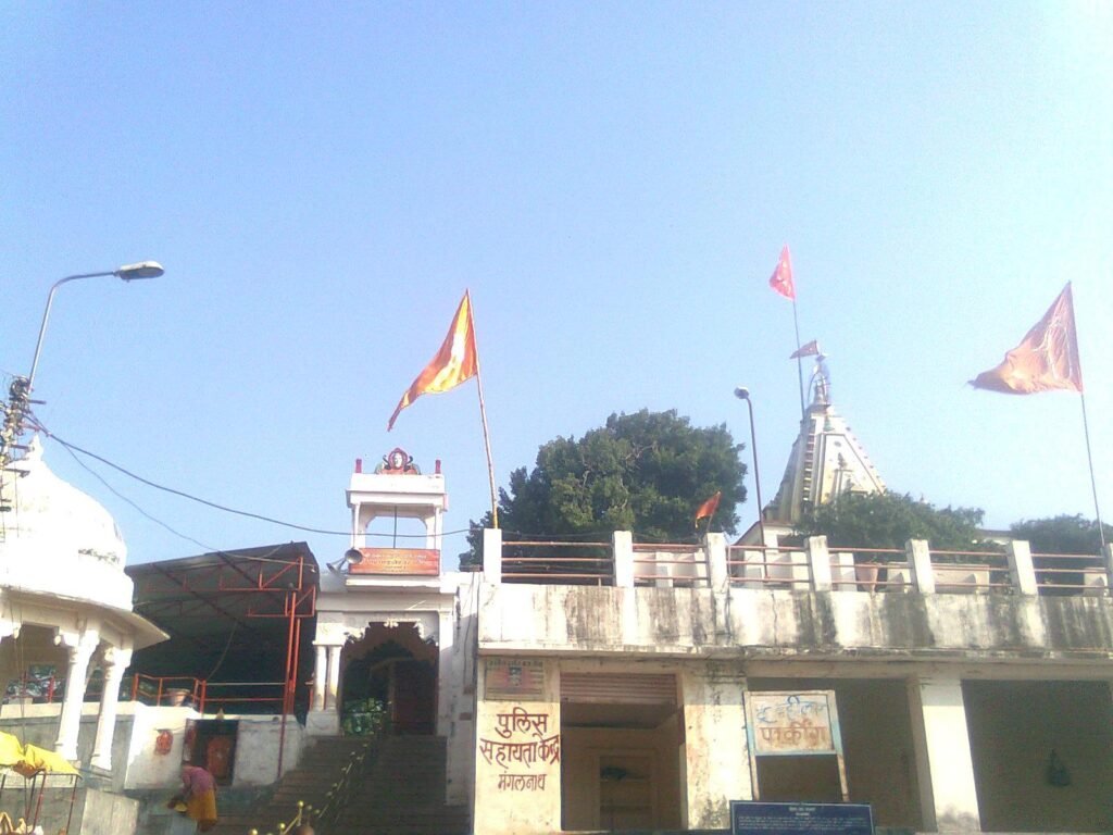 The white shikhara and saffron flags of the Mangalnath Temple in Ujjain under a clear sky.