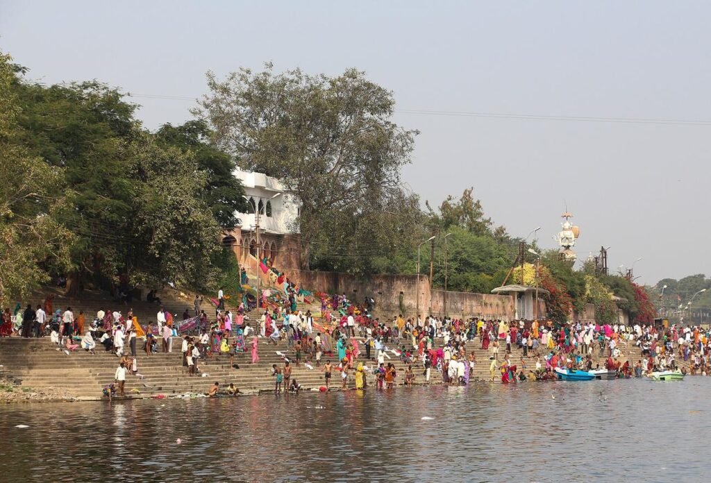 Pilgrims on the long steps of Ram Ghat beside the Shipra river in Ujjain, with trees and temples above.